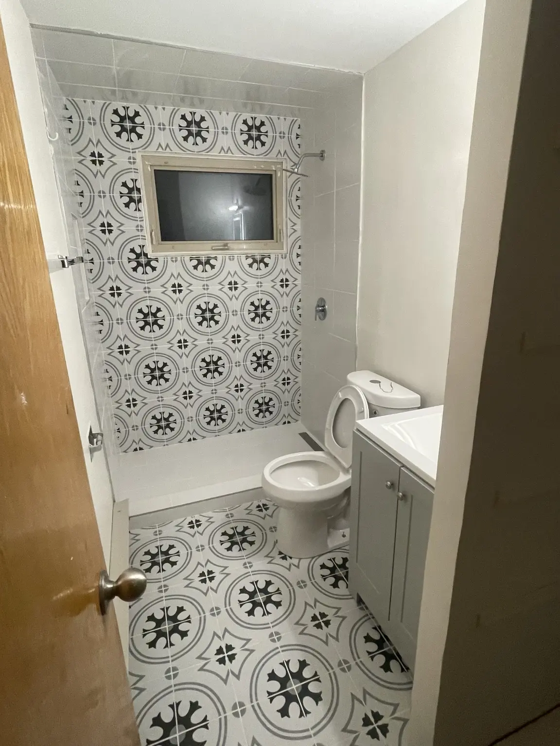 Wider finished bathroom view showing the patterned tile floor and shower wall
