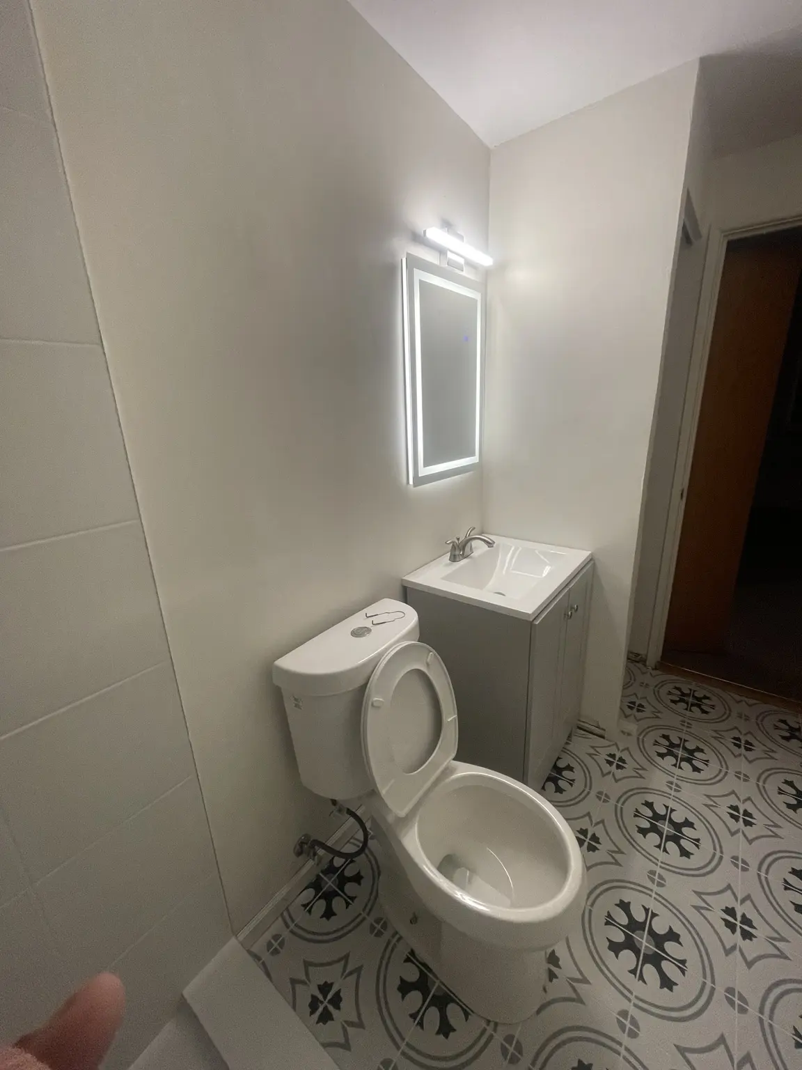 Finished bathroom vanity, toilet and illuminated mirror with patterned tile floor